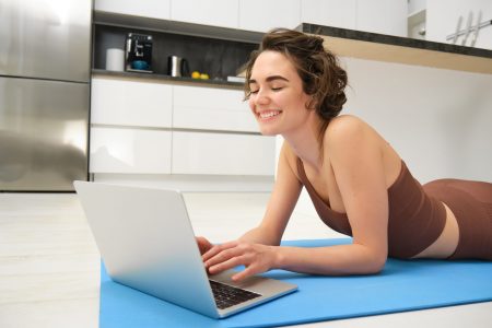 Portrait of beautiful sportswoman, fitness girl watching videos on laptop during workout, follow online pilates videos while exercise at home, wearing activewear in kitchen.